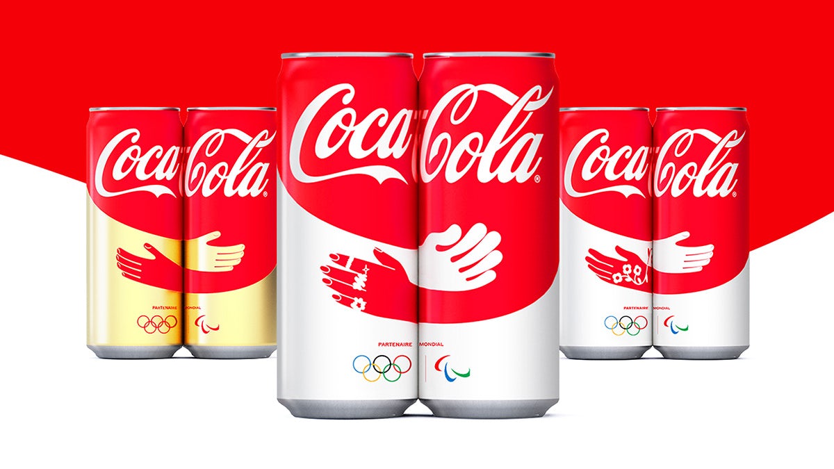 Line of up three pairs of Coca-Cola cans each displaying an illustration of hands embracing across two cans when placed together in pairs, creatd for Paris 2024 Olympics