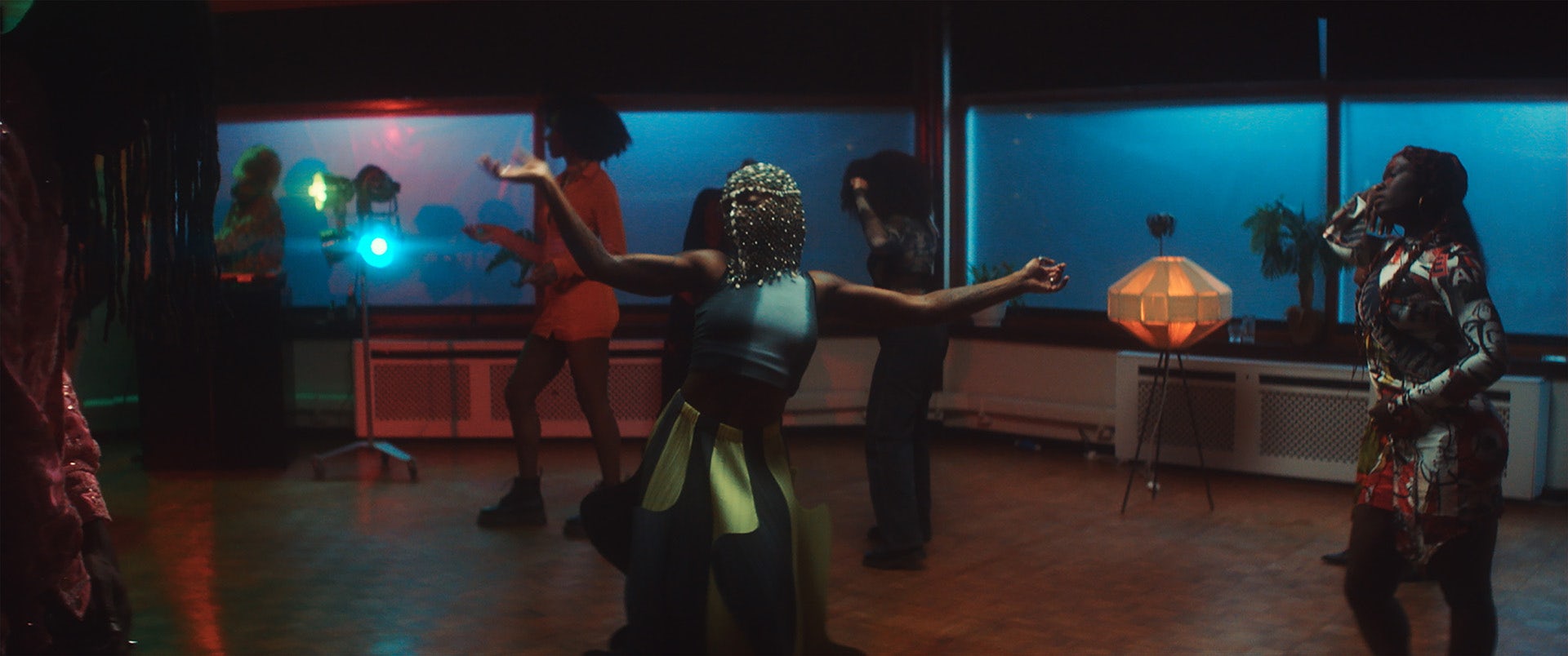 A person wearing a jewelled head covering dancing in a dimly lit room with other people in the background