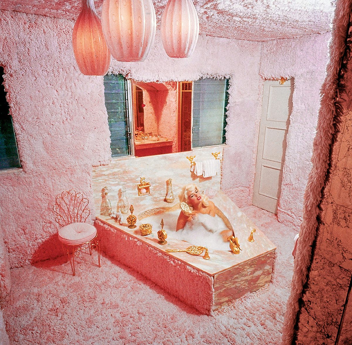 A woman in a foamy bath in a room covered in pink fluffy decor