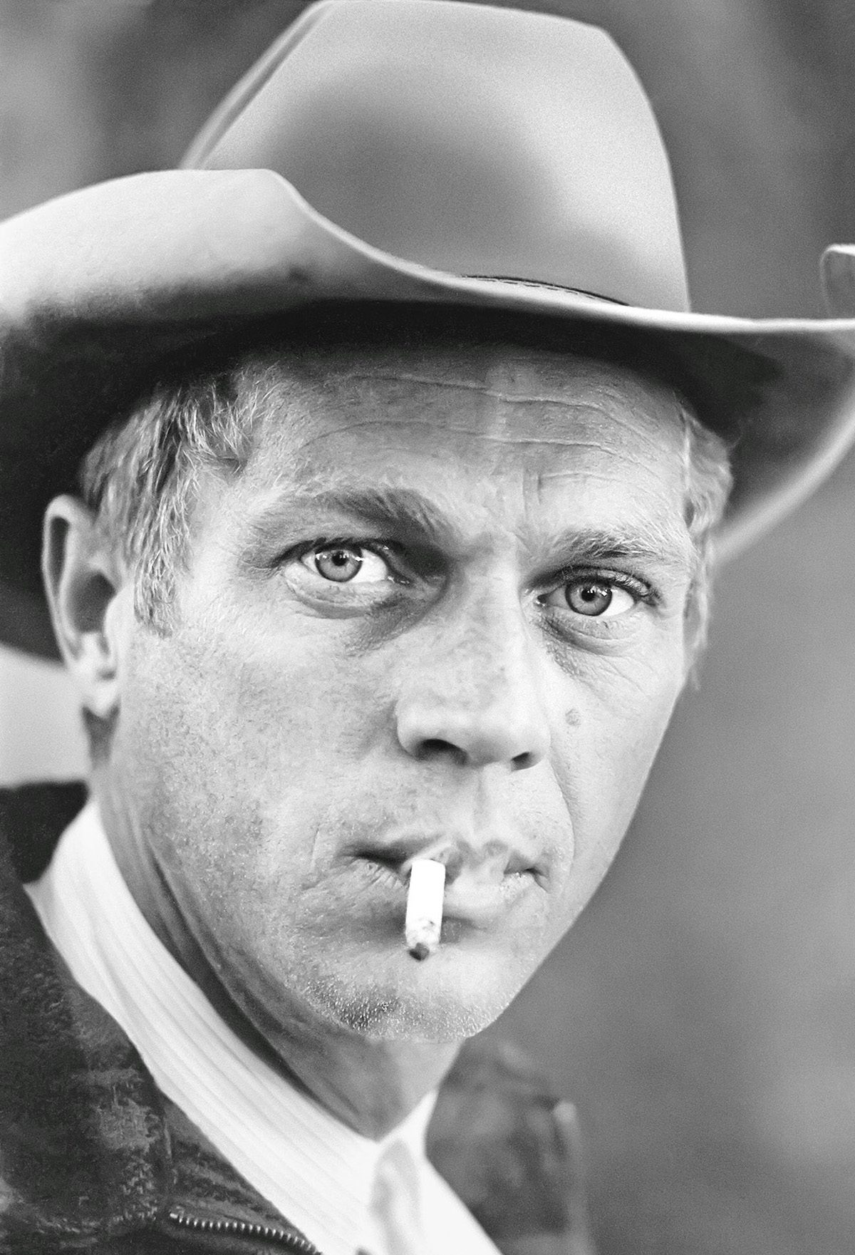 Black and white photo of actor Steve McQueen wearing a stetson and smoking a cigarette looking at the camera