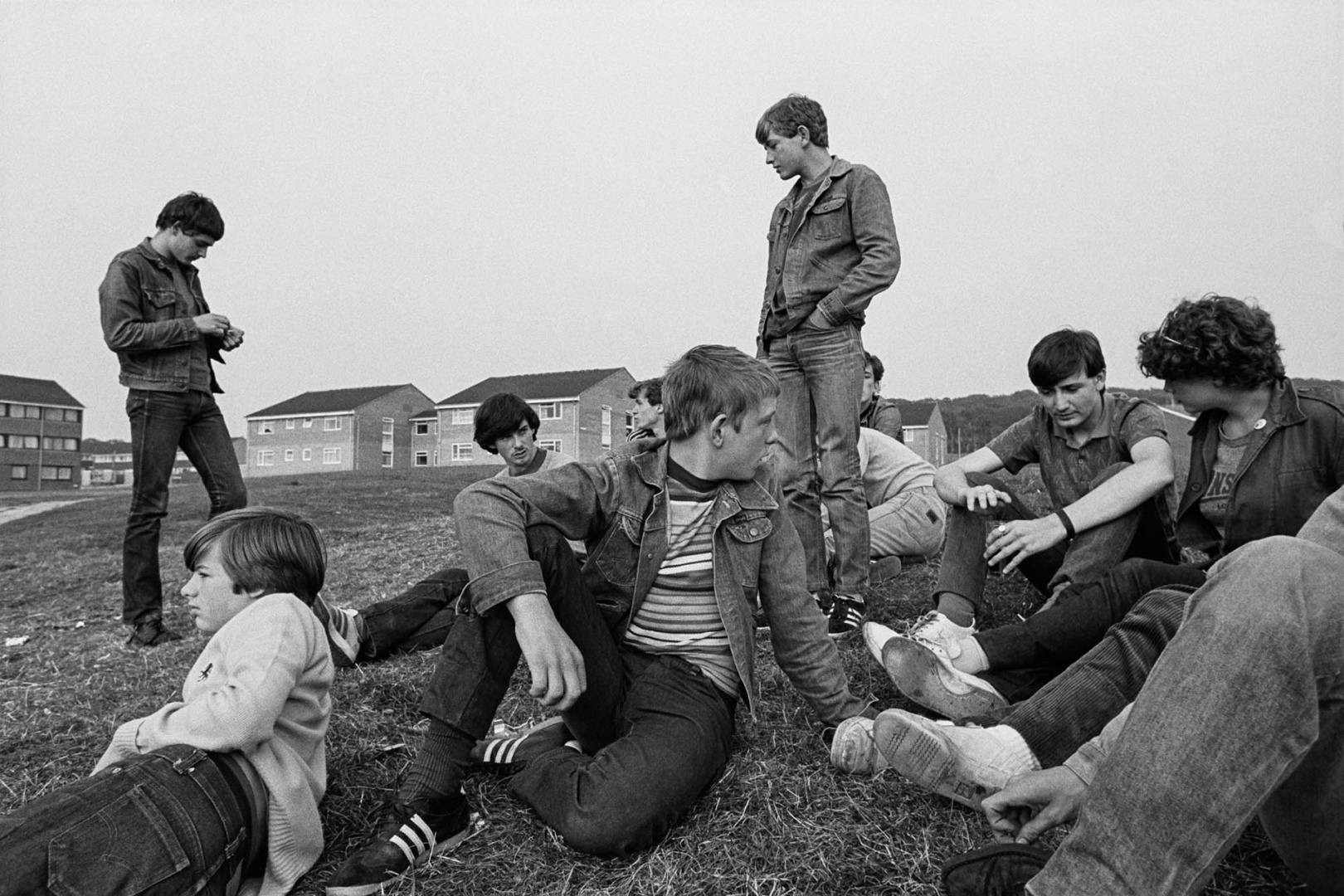 Black and white photo of a group of young adults sat on a grassy mound in front of rows of houses