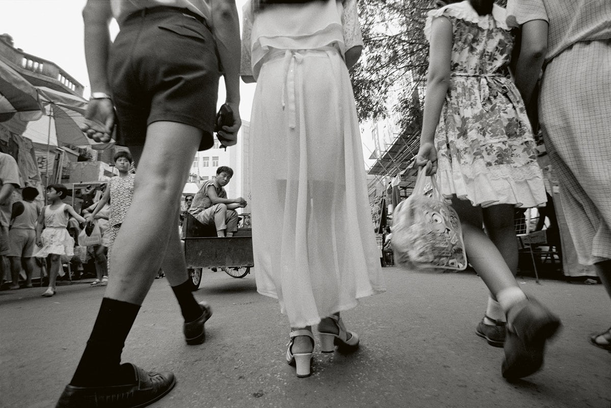 Black and white photo by Mo Yi taken from ground level showing the lower half of three people walking in a street 