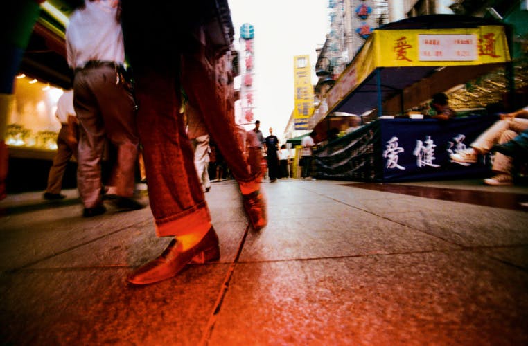 Red hued photograph by Mo Yi of a street scene featuring a person's legs and feet taken near ground level