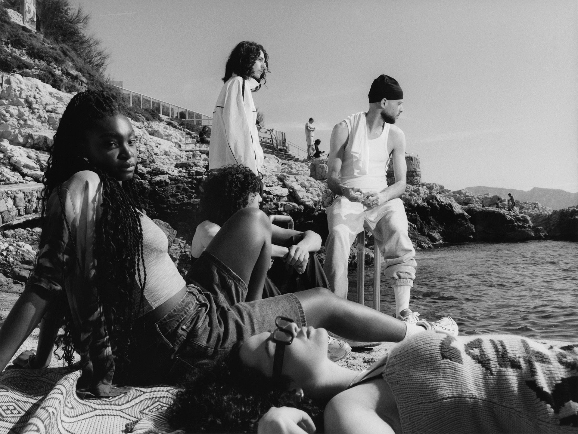 Black and white shot of a group of young people lounging on a rocky coastline near the water